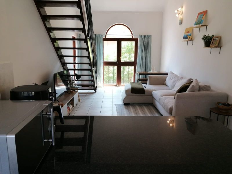 Open-plan living area featuring a modern staircase, granite kitchen countertop, and an arched glass door leading to a balcony.