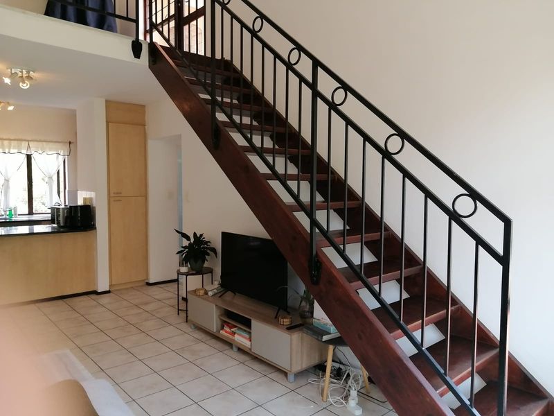 Open plan living area featuring a wooden staircase with wrought iron balustrade, tiled flooring, and an adjacent kitchen space.