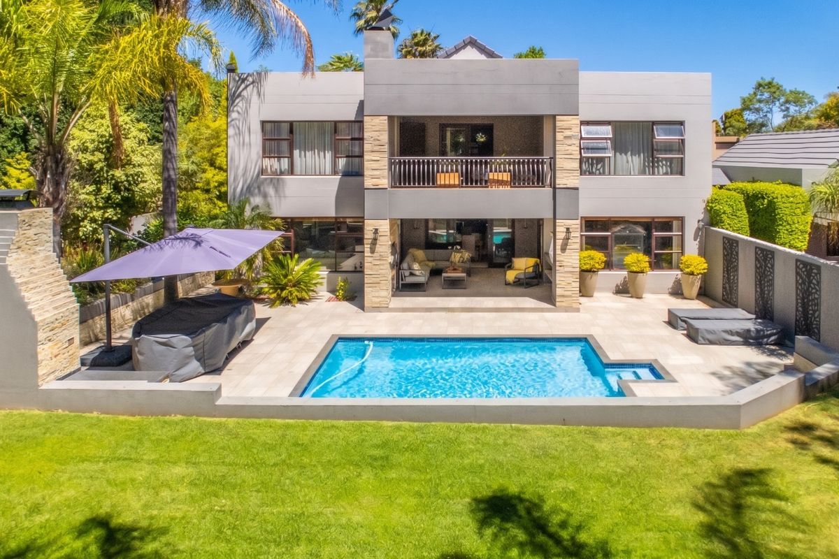 Rear view of a modern two-story house featuring a swimming pool, paved patio area, built-in outdoor fireplace, and an upper-level balcony.