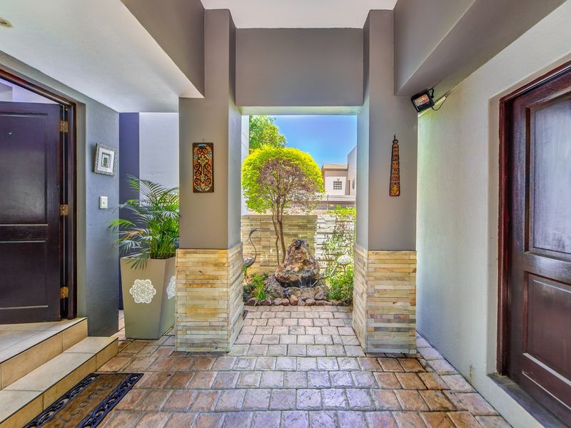 Inviting entrance foyer featuring stone-clad pillars, paved flooring, and a tranquil built-in water feature, creating a sophisticated welcome to the home.