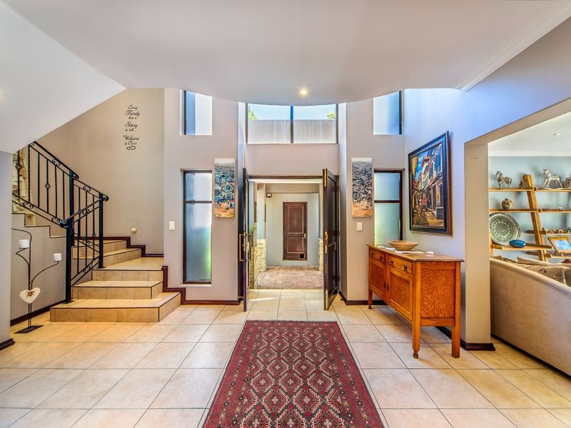 Spacious double-volume entrance hall featuring tiled flooring, a wrought iron staircase, and abundant natural light through vertical windows.
