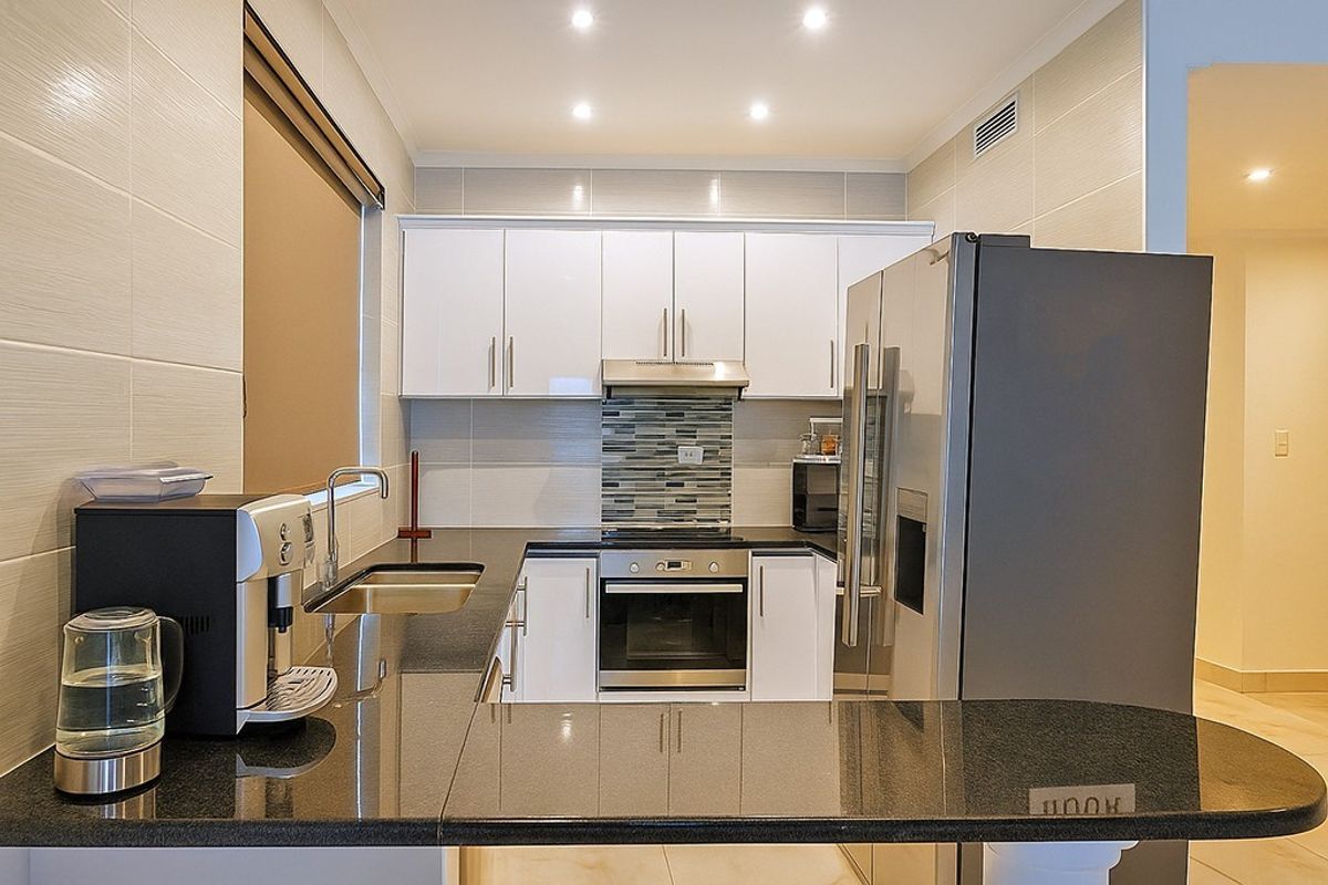 Modern kitchen featuring white cabinetry, dark granite countertops, stainless steel appliances, and a tiled backsplash with recessed lighting.