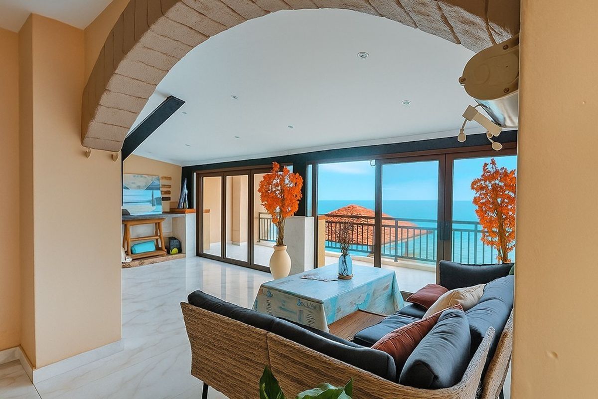Spacious living area featuring a distinctive stone archway, marble flooring, and large sliding glass doors that open to a balcony with ocean views.