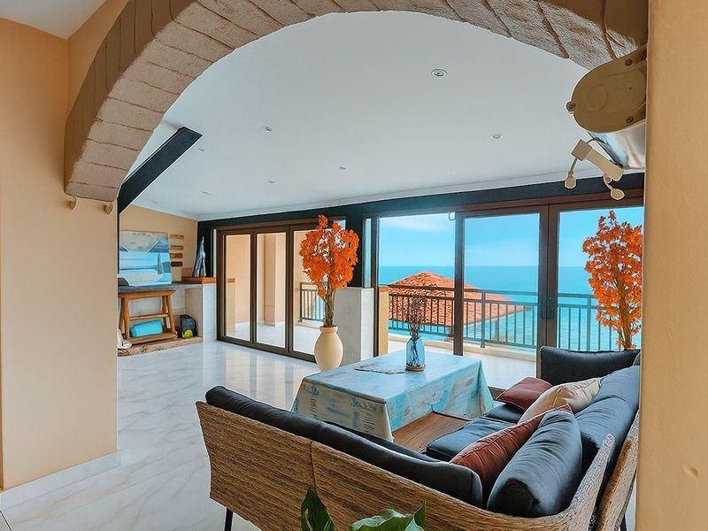 Spacious living area featuring a distinctive stone archway, marble flooring, and large sliding glass doors that open to a balcony with ocean views.