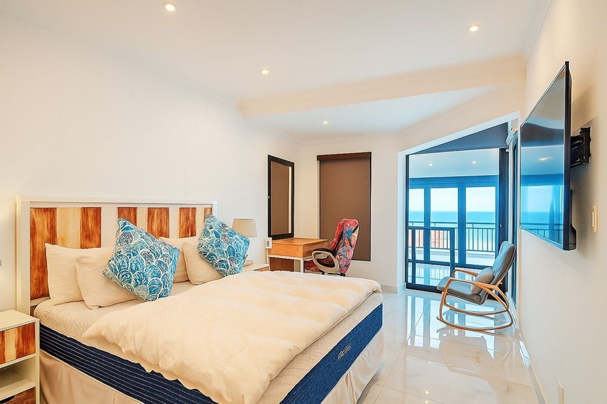 A bright and modern bedroom featuring tiled flooring, recessed lighting, and direct access to a private balcony with ocean views.