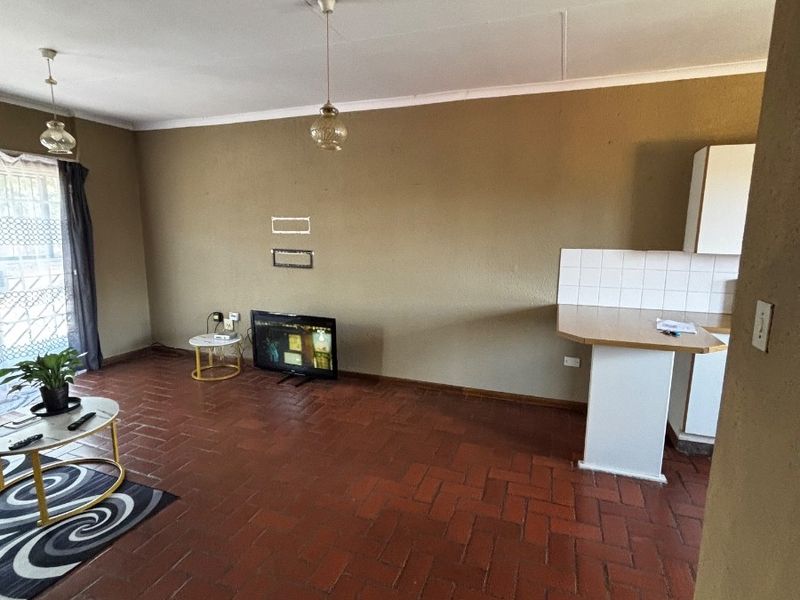 Open plan living and kitchen area featuring terracotta tile flooring, a breakfast bar with tiled splashback, and direct access to an outdoor security gate.