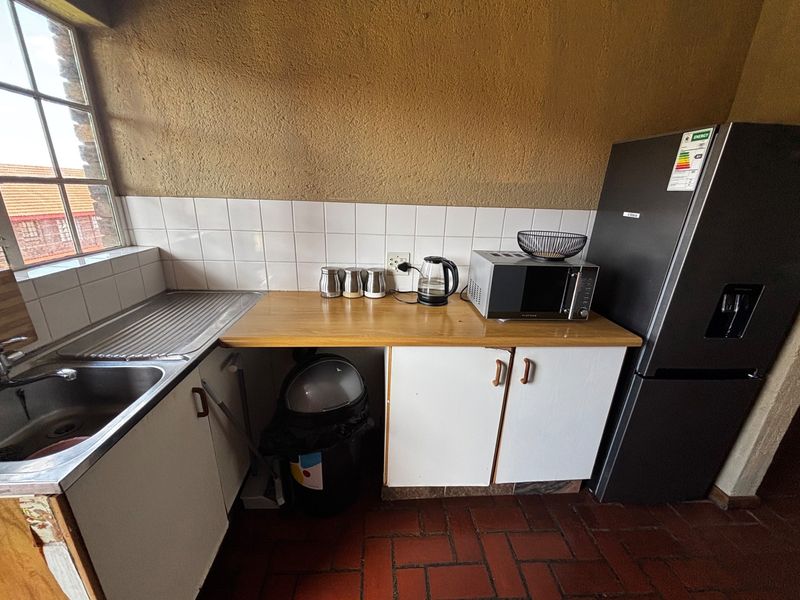 A compact kitchen area featuring a stainless steel sink, tiled backsplash, laminate countertops, and built-in cabinetry with terracotta floor tiles.