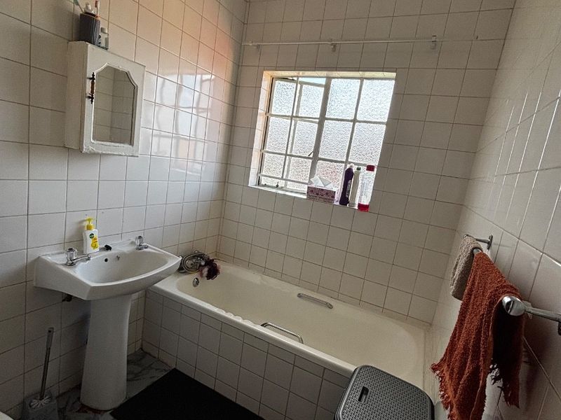 A dated bathroom featuring a pedestal basin, built-in bathtub, and wall-mounted medicine cabinet, finished with full-height wall tiling.