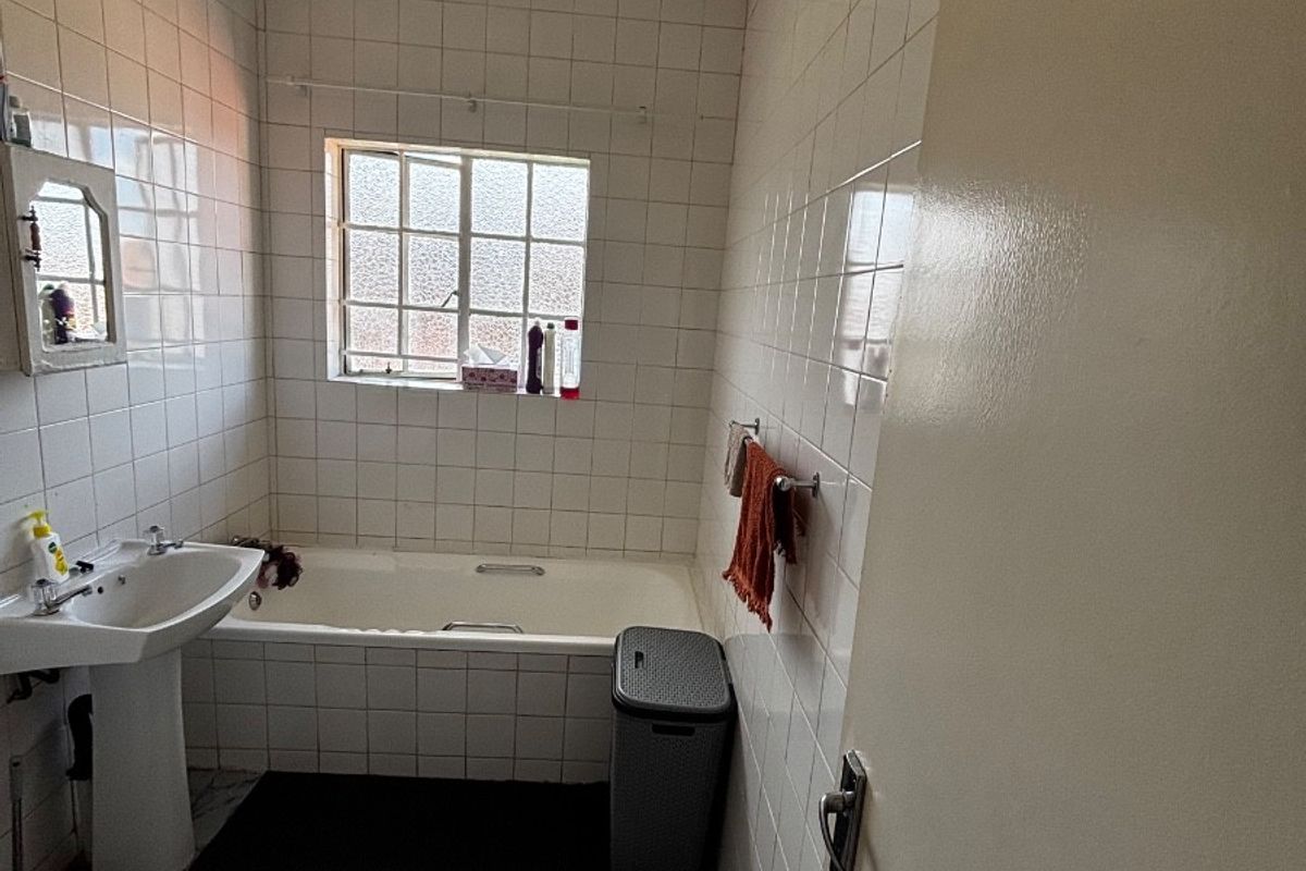 A functional bathroom featuring a pedestal washbasin, a built-in bathtub, and full-height wall tiling, offering potential for a modern renovation.