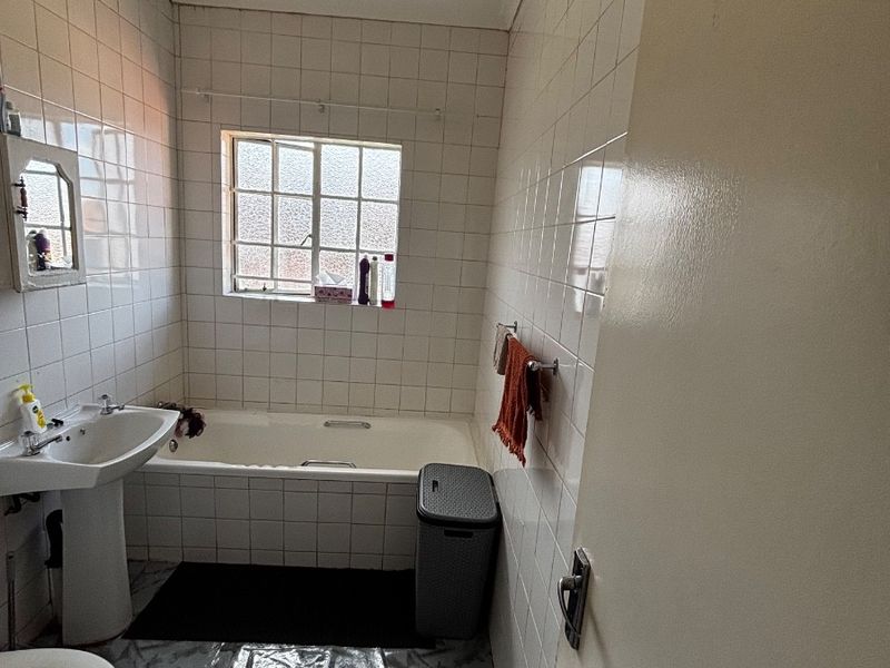 A functional bathroom featuring a pedestal washbasin, a built-in bathtub, and full-height wall tiling, offering potential for a modern renovation.