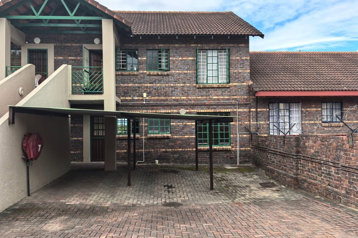 Front exterior view of a multi-story brick apartment building featuring a paved driveway, covered carport, and security-enhanced windows.