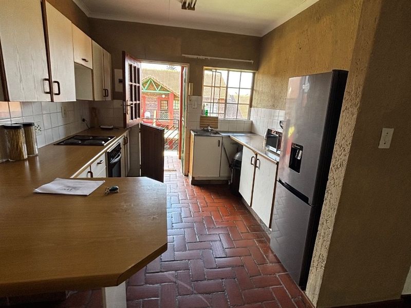 Functional kitchen featuring built-in cabinetry, laminate countertops, integrated appliances, and durable terracotta floor tiles with direct access to an outdoor area.