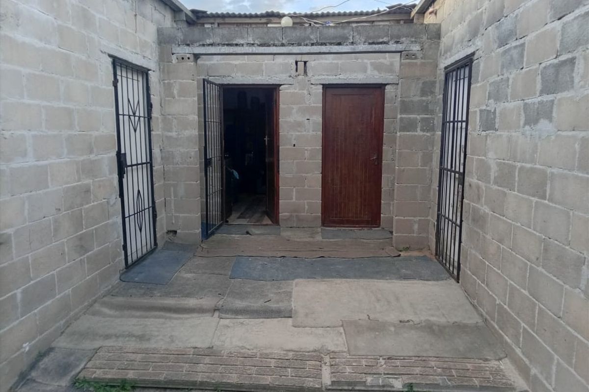 An enclosed rear courtyard featuring unfinished concrete block walls, security gates, and multiple access doors, requiring significant finishing and maintenance.