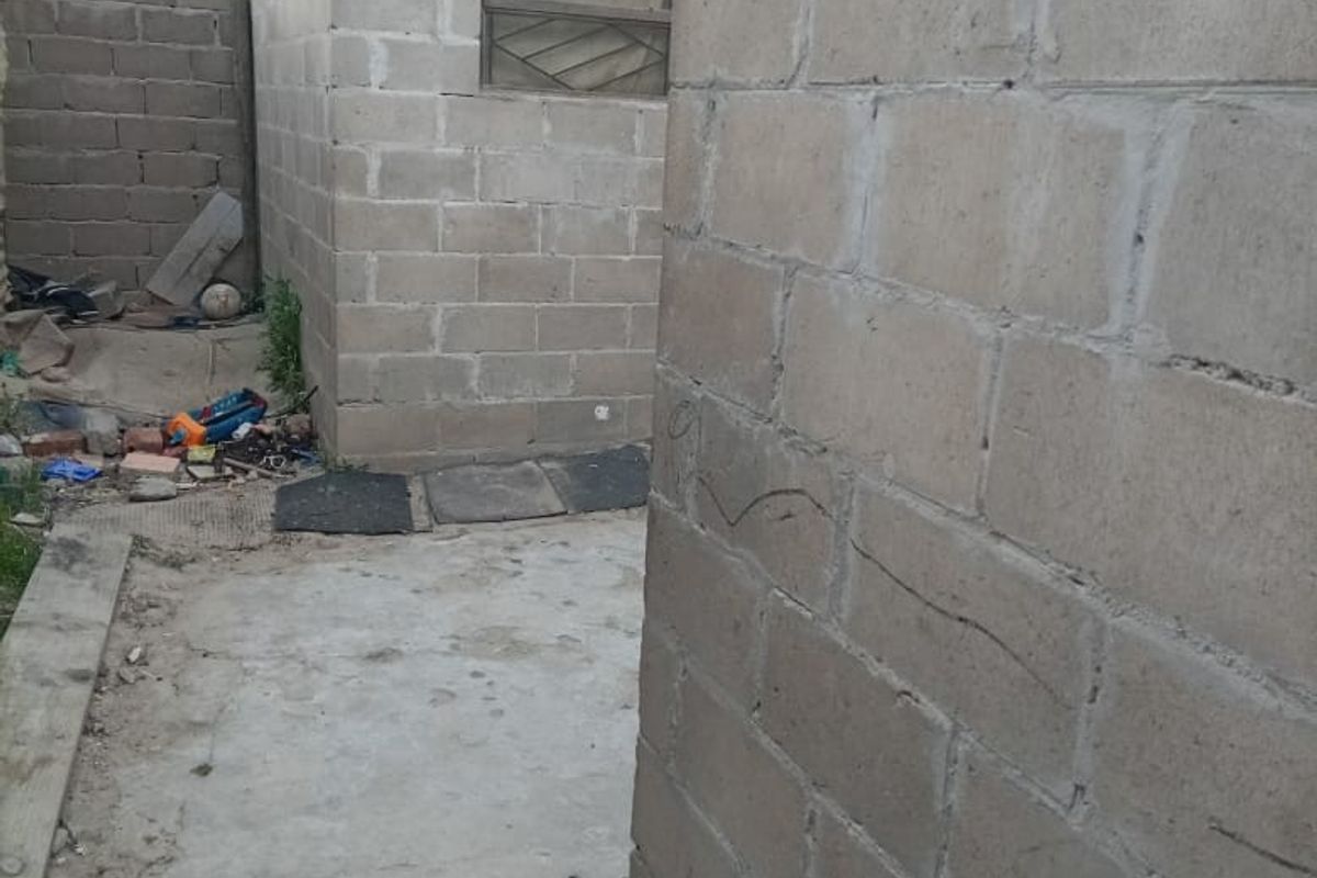 A view of the rear exterior area featuring unfinished concrete block walls and basic concrete paving, requiring maintenance and landscaping.