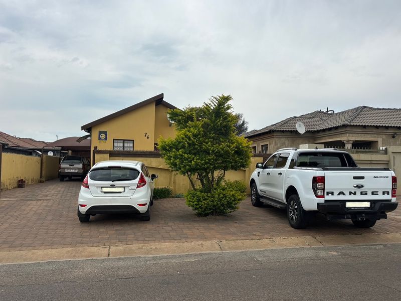 Front exterior view of the property featuring a paved driveway, boundary wall with security spikes, and a carport.