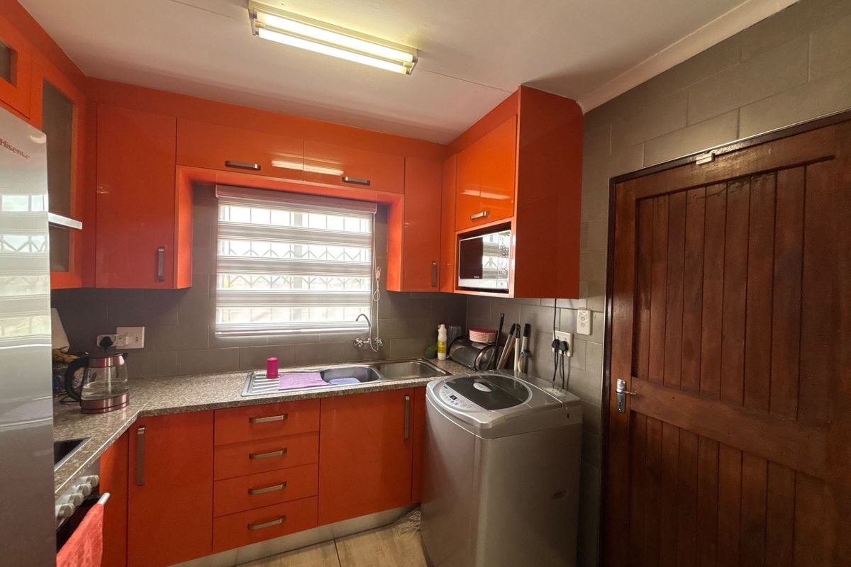 A functional kitchen featuring vibrant orange cabinetry, a stainless steel sink, tiled backsplash, and built-in microwave, providing efficient storage and workspace.