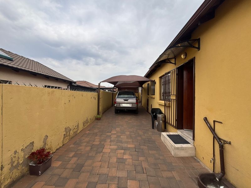 A paved side driveway featuring a carport, boundary wall, and secure entrance access to the property.