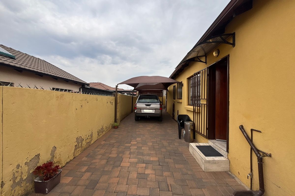 A paved side driveway featuring a carport, boundary wall, and secure entrance access to the property.