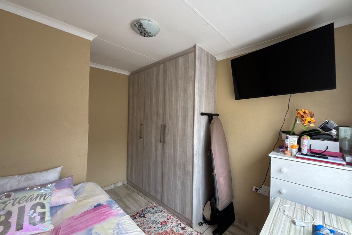 A functional bedroom featuring a built-in wardrobe, laminate flooring, and neutral wall finishes, providing a practical and comfortable living space.