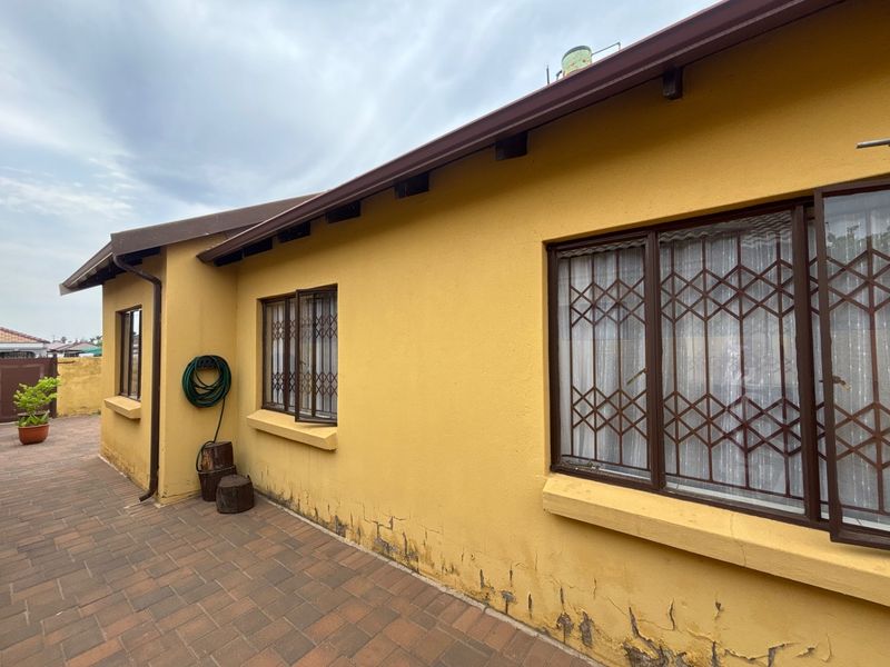 Rear exterior view of the house featuring a paved patio area, security bars on windows, and visible wear to the exterior wall plaster.