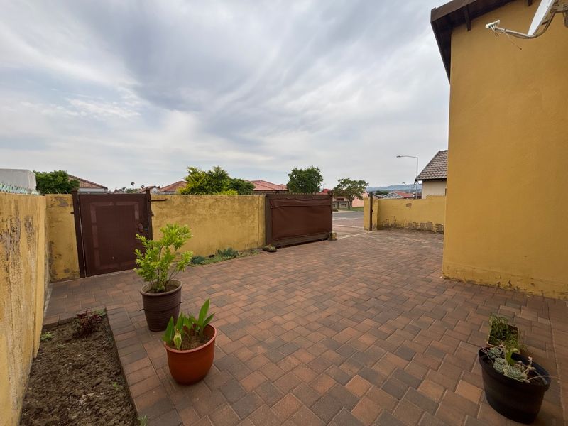 A paved front driveway area featuring a boundary wall with metal gate access and exterior security camera.