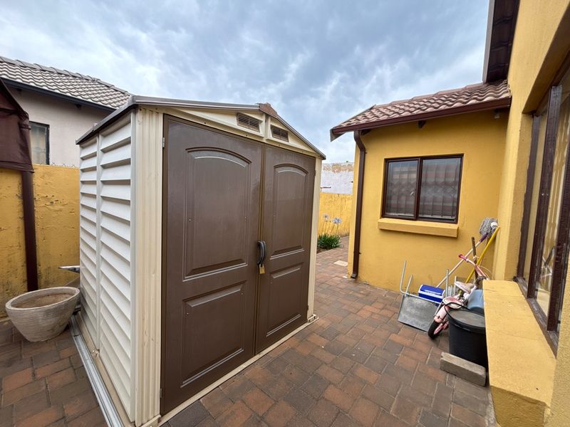 A paved rear courtyard area featuring a plastic storage shed and access to the main dwelling with security-barred windows.
