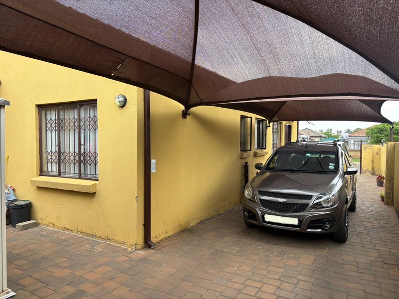 Outdoor parking area featuring a paved driveway and a large shade sail structure providing cover for vehicles.