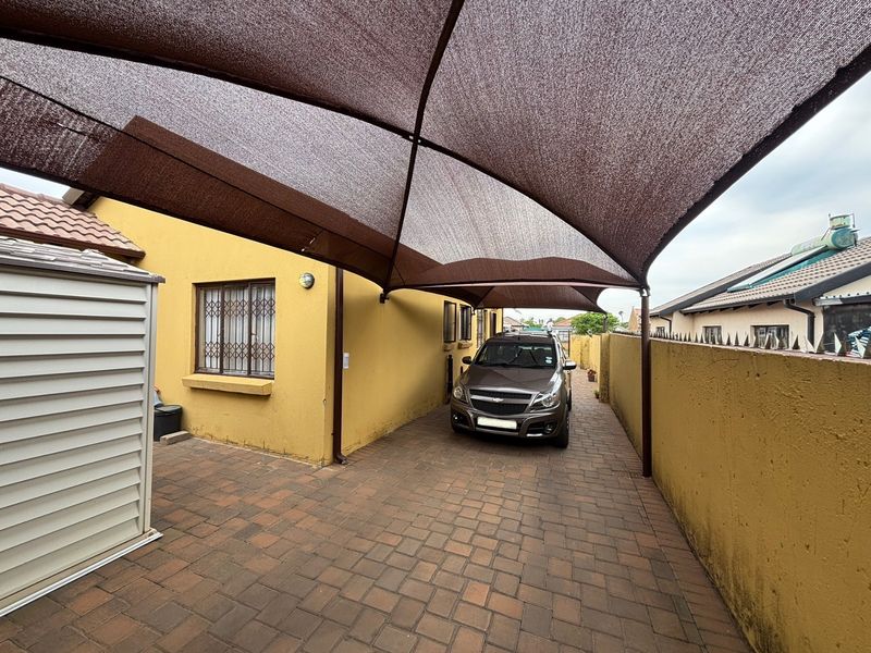 A paved driveway area featuring a large shade cloth carport, secure window bars, and a metal storage shed along the boundary wall.