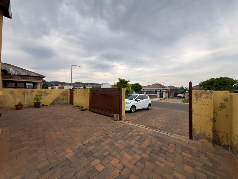 Front exterior view of the property featuring a paved driveway, sliding gate with motor, and a boundary wall requiring maintenance and repainting.