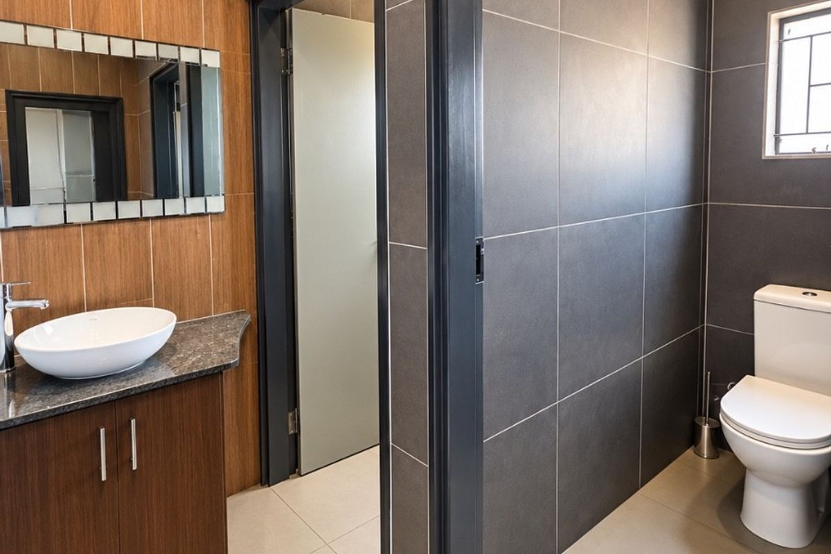 Modern bathroom featuring a wood-finish vanity with a vessel sink, granite countertop, and dark tiled walls, offering a clean and contemporary aesthetic.