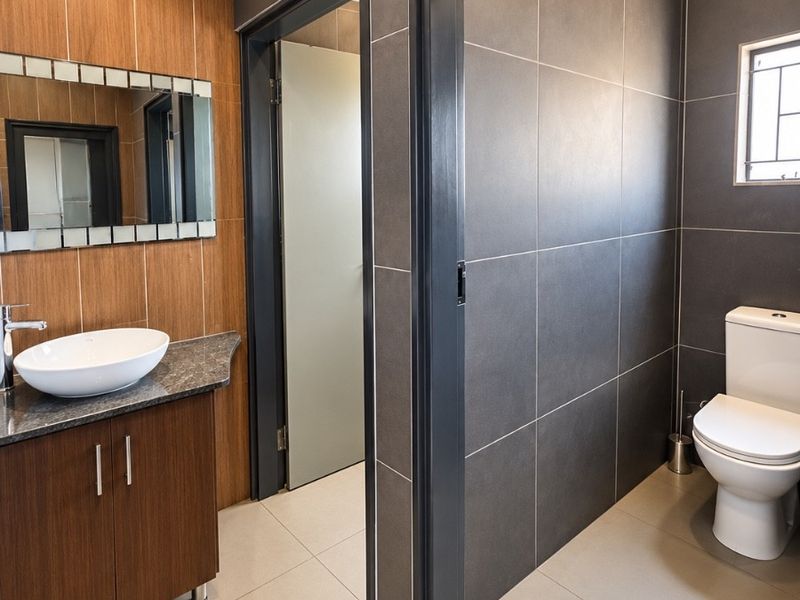 Modern bathroom featuring a wood-finish vanity with a vessel sink, granite countertop, and dark tiled walls, offering a clean and contemporary aesthetic.