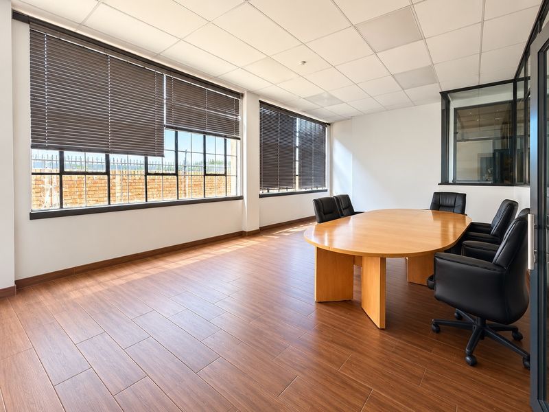A bright and professional office space featuring wood-look tile flooring, a suspended ceiling, and large windows with venetian blinds, offering a clean, modern workspace.
