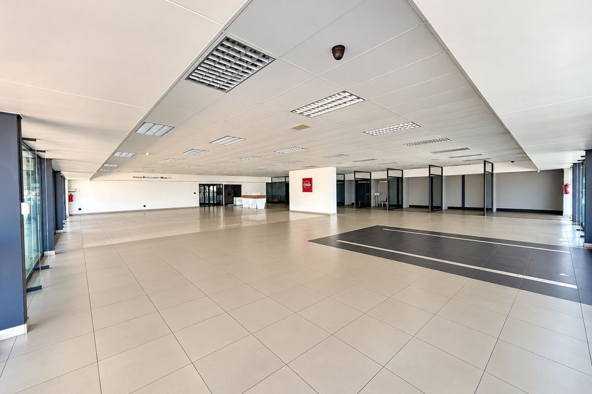 A spacious, open-plan commercial showroom featuring high-quality ceramic tiling, a modern suspended ceiling with recessed lighting, and glass-partitioned office or display areas.