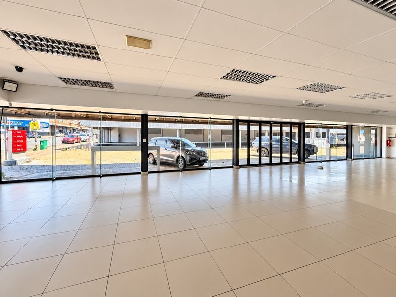 Spacious open-plan commercial showroom featuring large glass sliding doors, tiled flooring, and a suspended ceiling with recessed lighting.