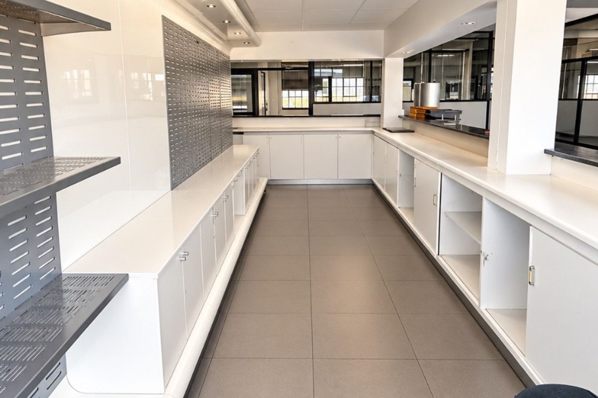 A clean, modern commercial kitchen or service area featuring extensive built-in cabinetry, tiled flooring, and integrated recessed lighting throughout the workspace.