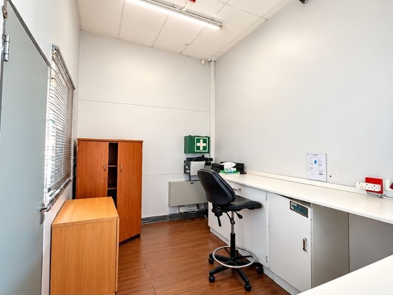 A functional commercial office space featuring a built-in desk, integrated cabinetry, laminate flooring, and a suspended ceiling with overhead lighting.