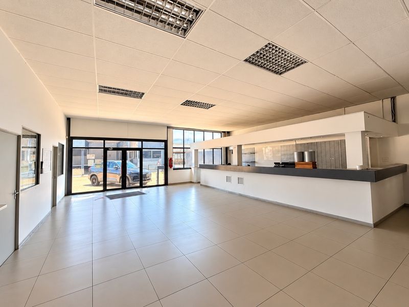Spacious open-plan commercial area featuring tiled flooring, a built-in service counter, and a suspended ceiling with recessed lighting, suitable for various business applications.