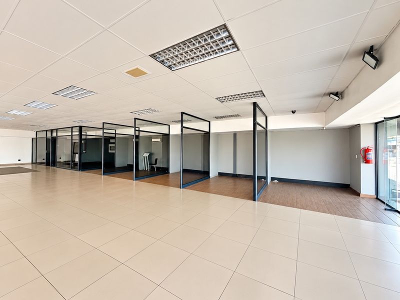 Spacious open-plan commercial office area featuring glass-partitioned private offices, modern tiled and wood-look flooring, and integrated suspended ceiling lighting.
