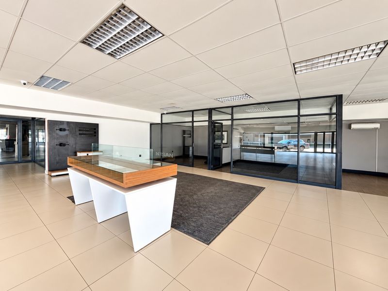 Spacious commercial office area featuring modern glass partitions, tiled flooring, and a suspended ceiling with integrated lighting.