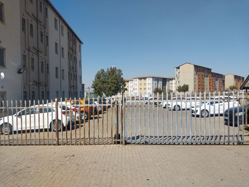 Exterior view of an apartment complex parking area featuring paved driveway and security fencing.