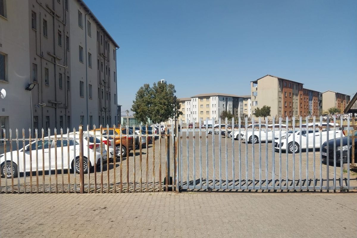 Exterior view of an apartment complex parking area featuring paved driveway and security fencing.