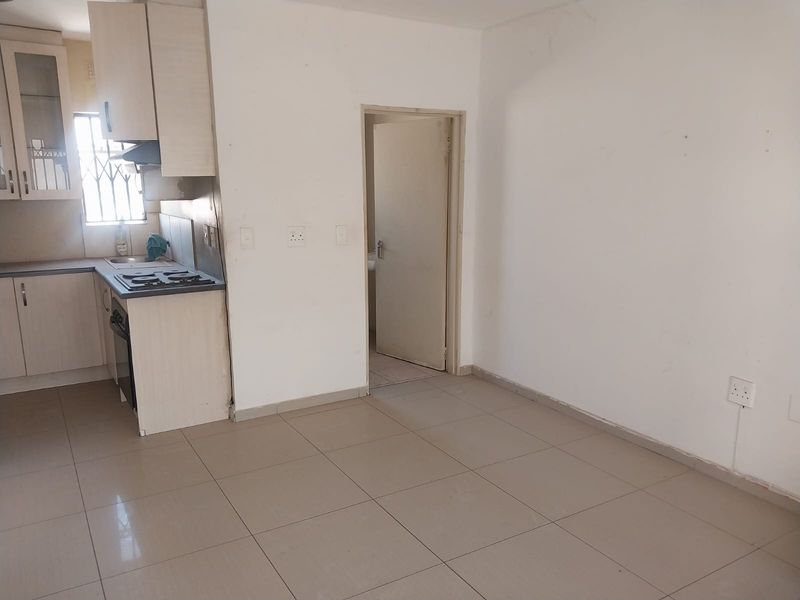 An open-plan living and kitchen area featuring tiled flooring, built-in cabinetry, and an integrated oven and hob, presenting a blank canvas for renovation.