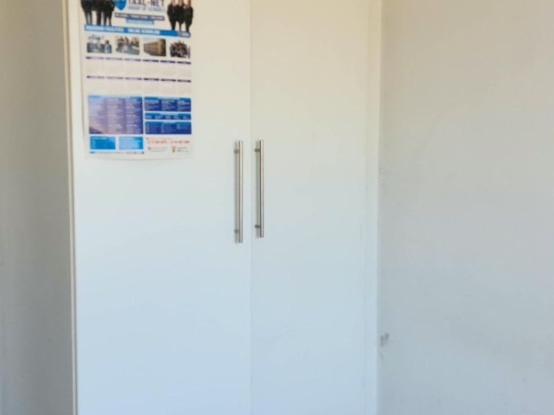 A bedroom featuring a white built-in wardrobe with integrated drawers and tiled flooring.