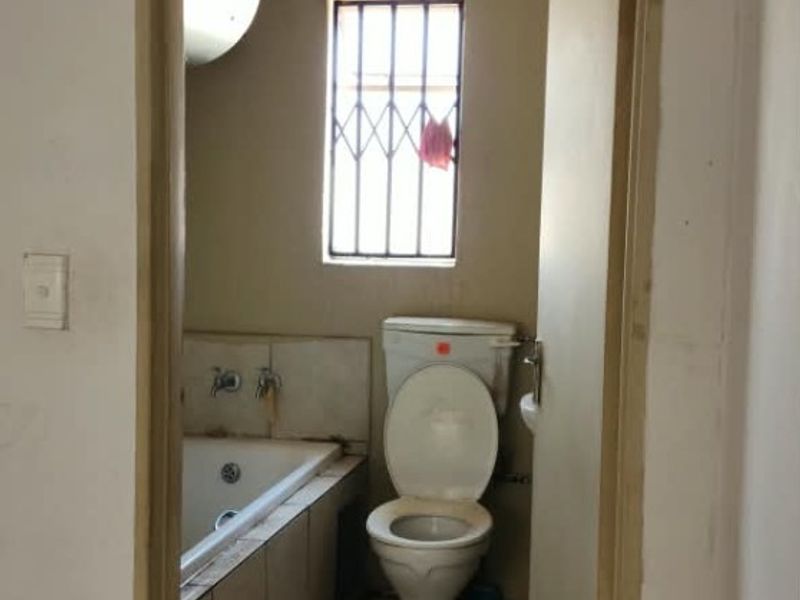 A dated bathroom featuring a built-in bathtub, toilet, and tiled flooring, requiring renovation to update the finishes and improve overall condition.