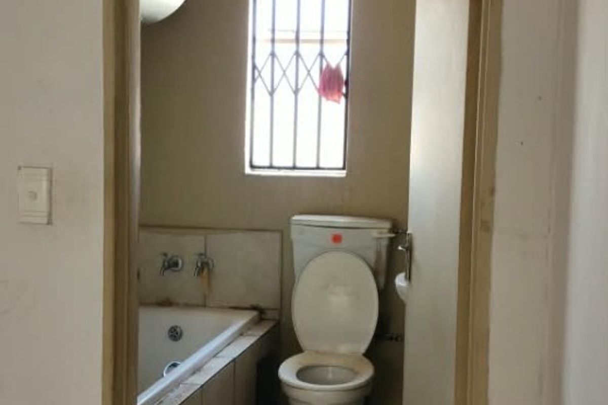 A dated bathroom featuring a built-in bathtub, toilet, and tiled flooring, requiring renovation to update the finishes and improve overall condition.