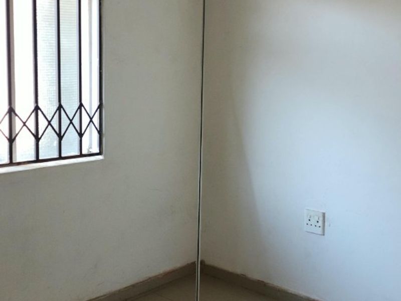 A vacant bedroom featuring tiled flooring, a security-gated window, and basic electrical fixtures, ready for a fresh coat of paint and new finishes.