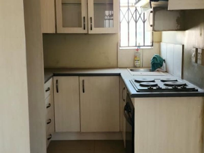 A compact kitchen featuring built-in cabinetry, laminate countertops, a built-in hob and oven, and tiled flooring.