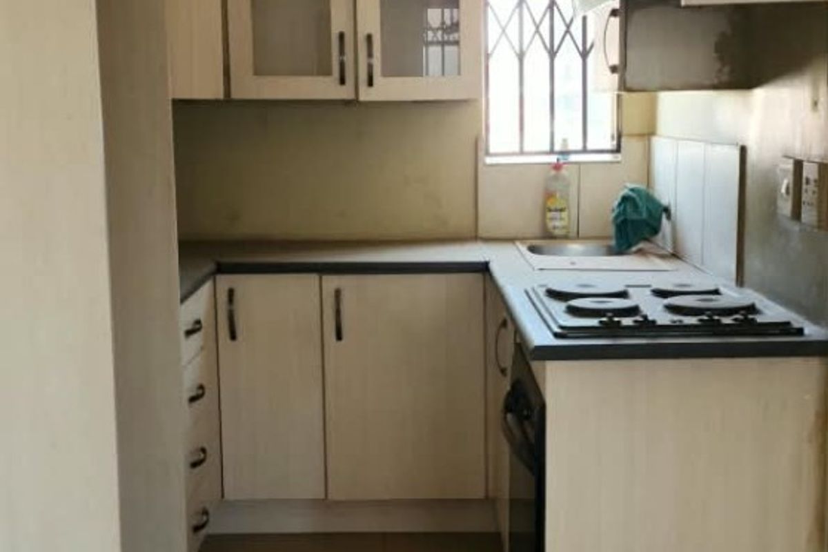 A compact kitchen featuring built-in cabinetry, laminate countertops, a built-in hob and oven, and tiled flooring.