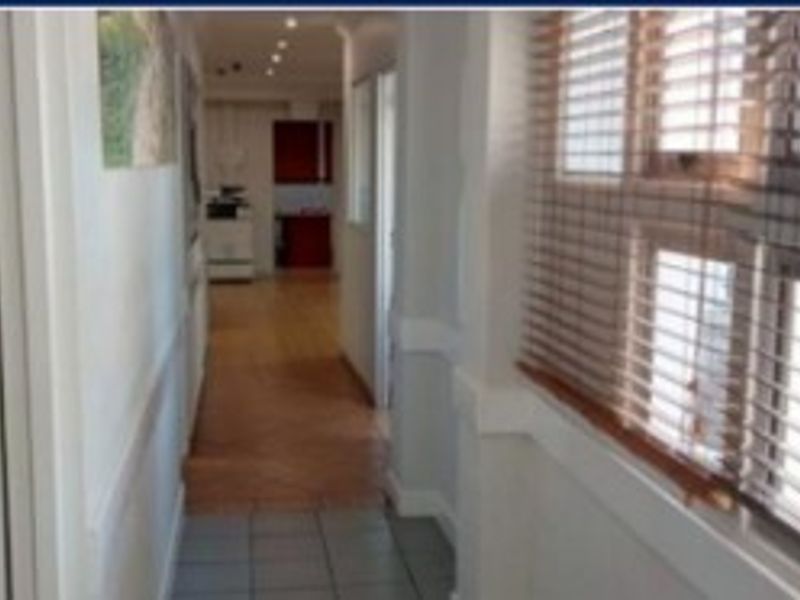 A functional office hallway featuring a mix of tiled and laminate flooring, recessed lighting, and window blinds.
