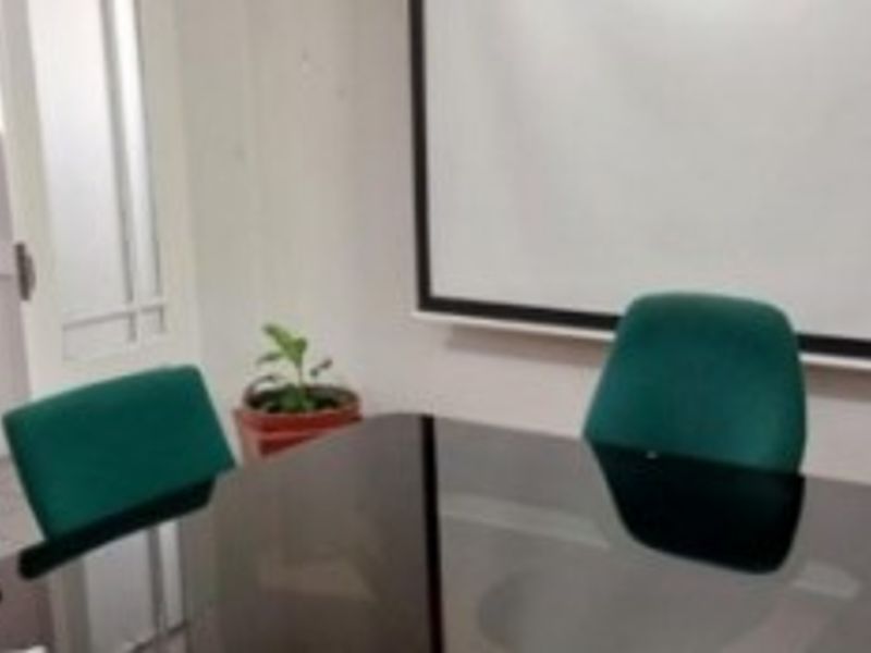 A functional office space featuring a wall-mounted projector screen and glass door access.